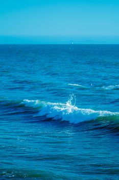 Peaceful ocean waves with splashing water under a clear blue sky, perfect for calm and zen themes.