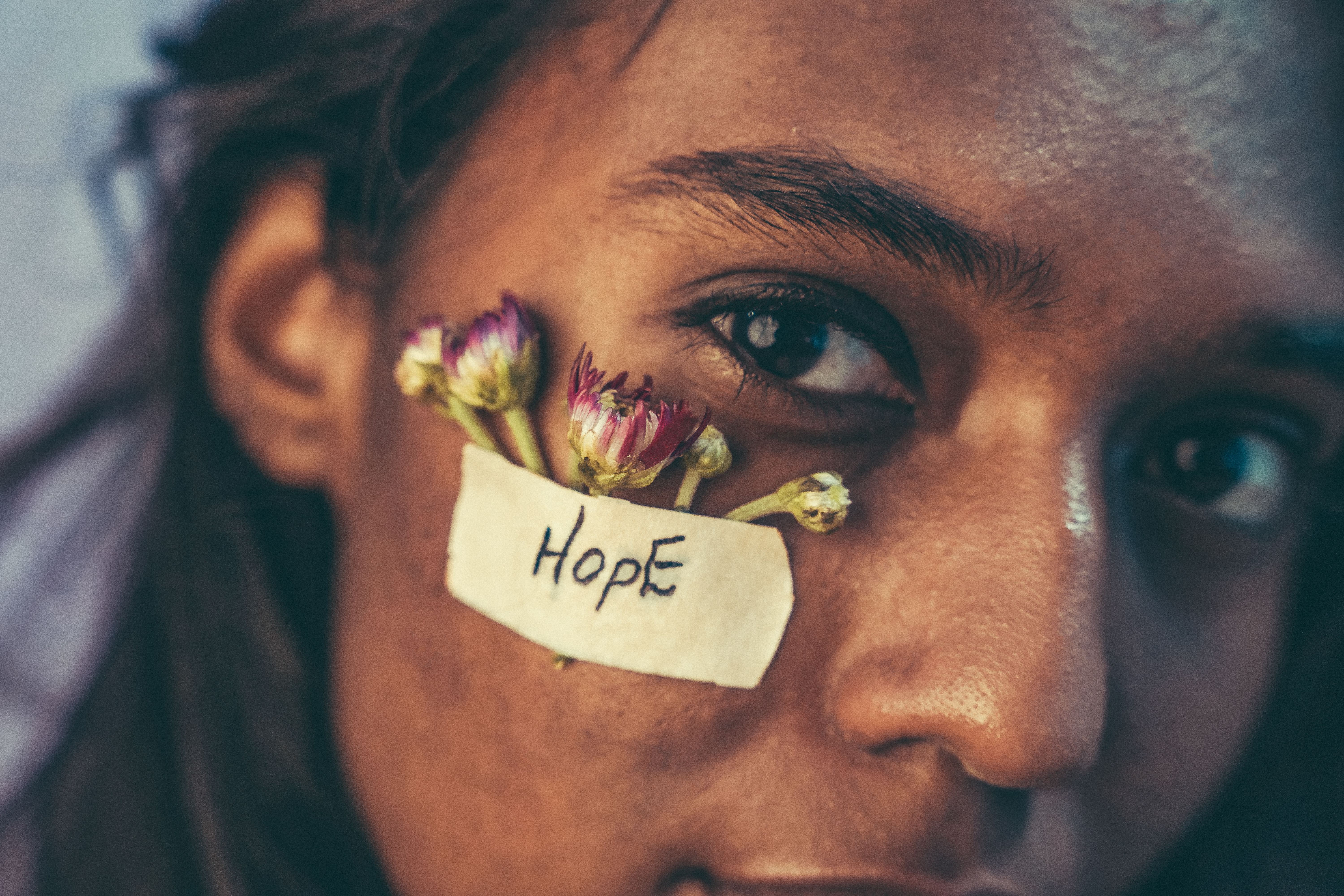 Retrato de uma pessoa com uma expressão de esperança, com flores e uma etiqueta escrita 'Hope' na face, simbolizando resiliência e esperança.