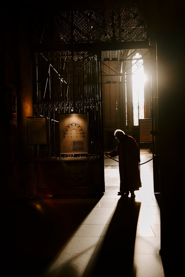 Silhouette Of Person Walking Through Iron Gate To Warehouse