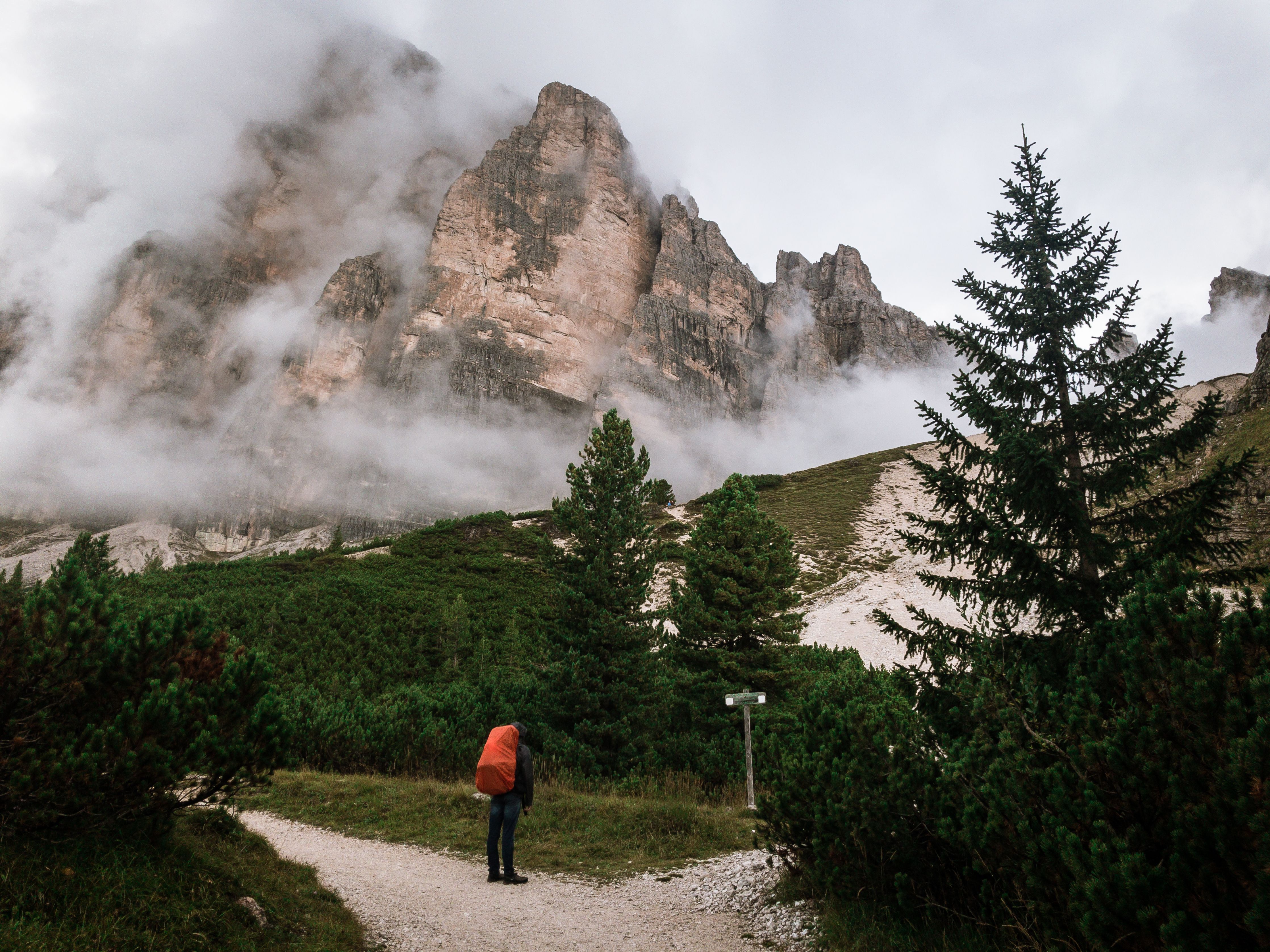 A lone hiker with a red backpack stands on a trail in the misty Dolomites, Cortina d’Ampezzo, Italy.
