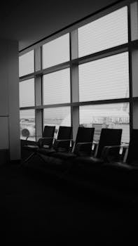Empty chairs in a quiet airport terminal in grayscale with window view.