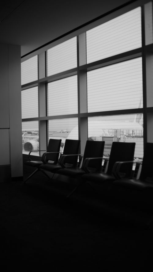 Free Empty chairs in a quiet airport terminal in grayscale with window view. Stock Photo