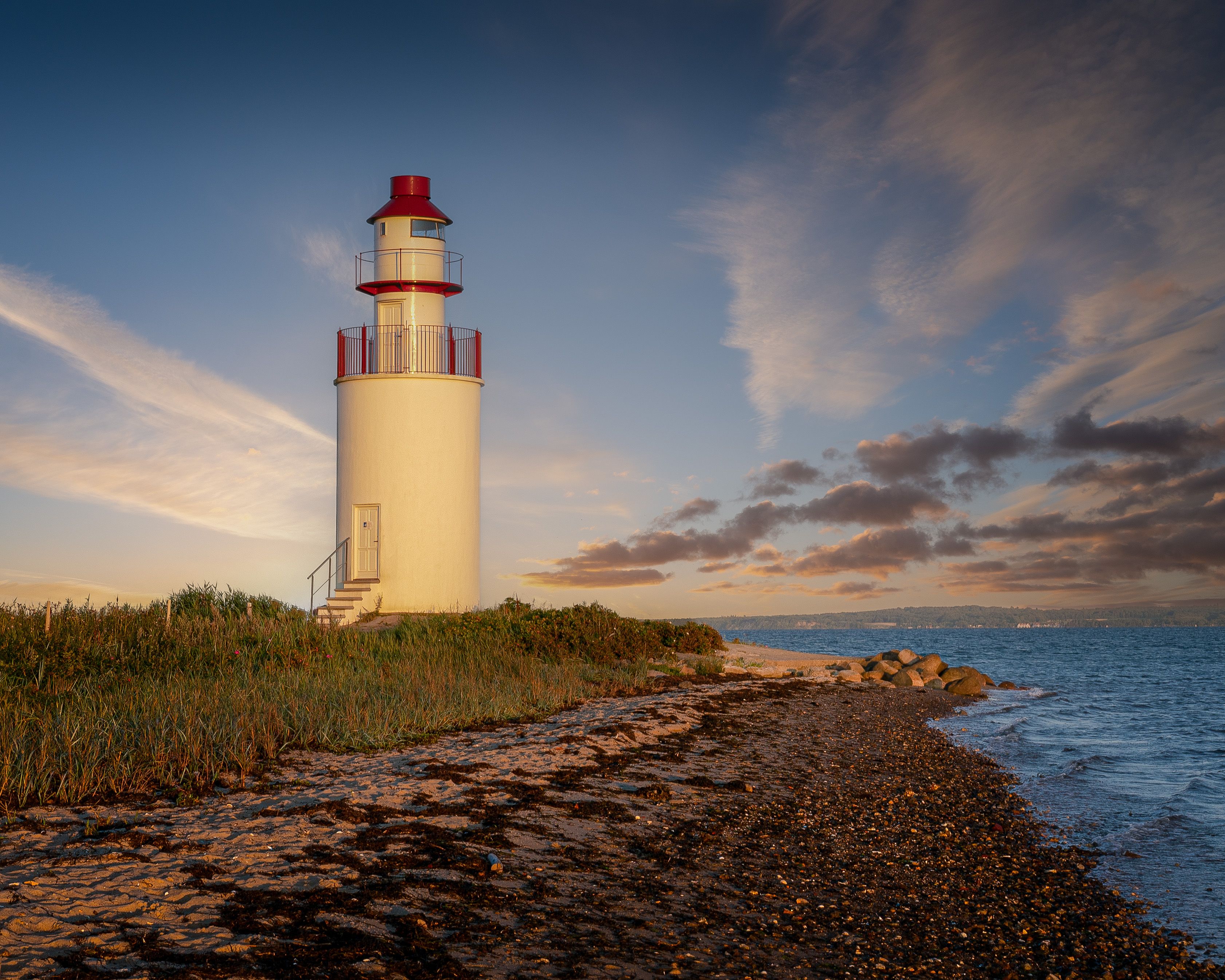 Scenic view of a lighthouse by the sea, capturing a peaceful sunset on Denmark's coastline.