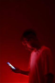 A blurry portrait of a man bathed in red light, using a smartphone in a dark setting.