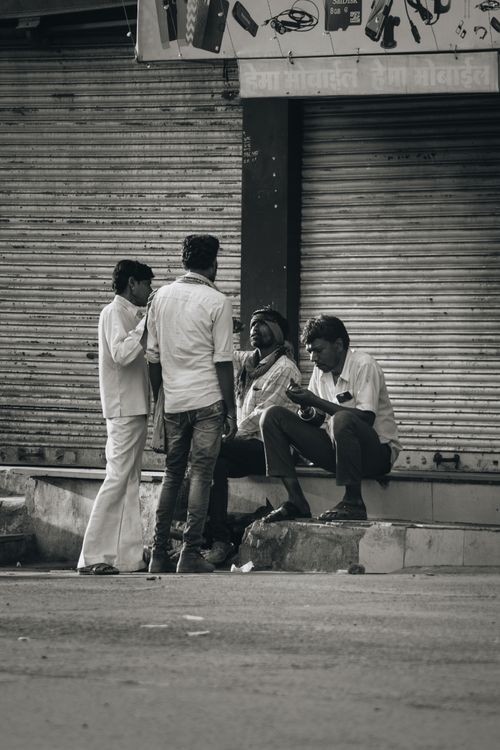 Free Four men gathered in conversation on a city street in a black and white urban setting. Stock Photo