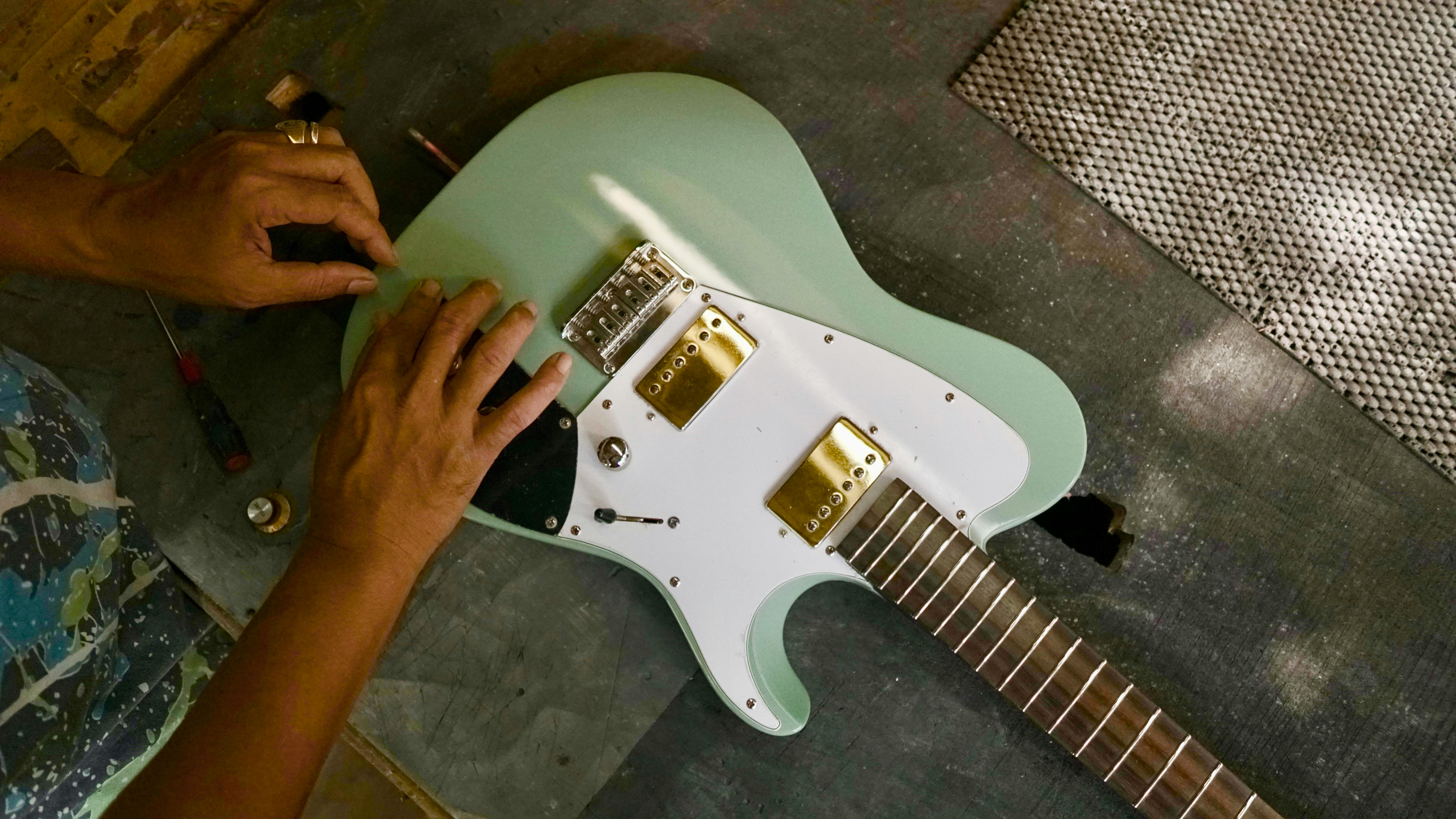 An artisan carefully assembling a mint green electric guitar in a workshop setting.