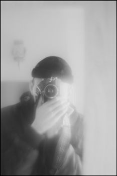A soft-focus black and white self-portrait capturing a photographer through a mirror.