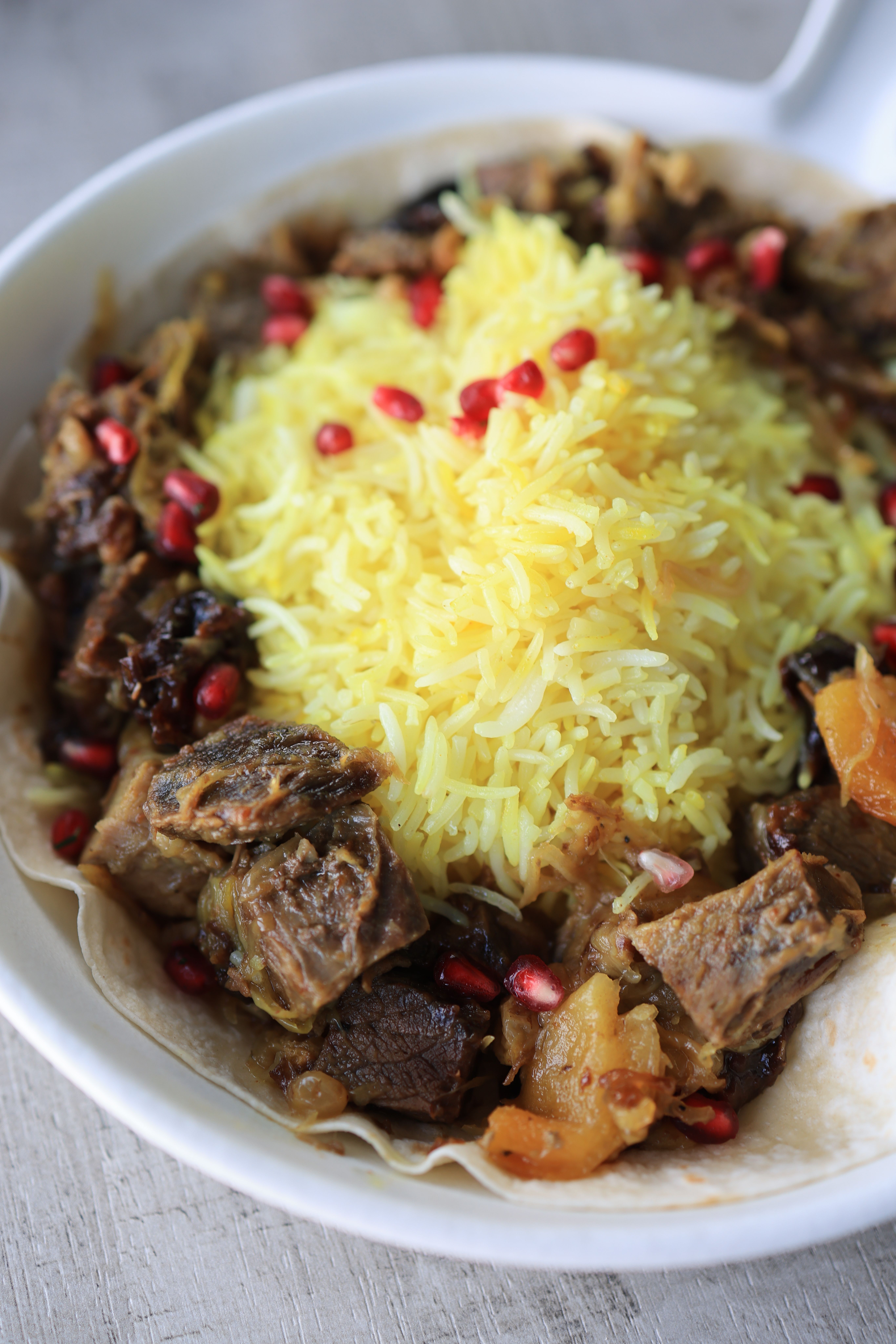 Saffron rice served with tender meat and pomegranate seeds, showcasing a vibrant culinary presentation.