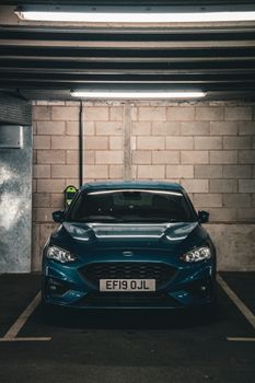 Front view of a blue car parked in an urban parking garage in Manchester, England.