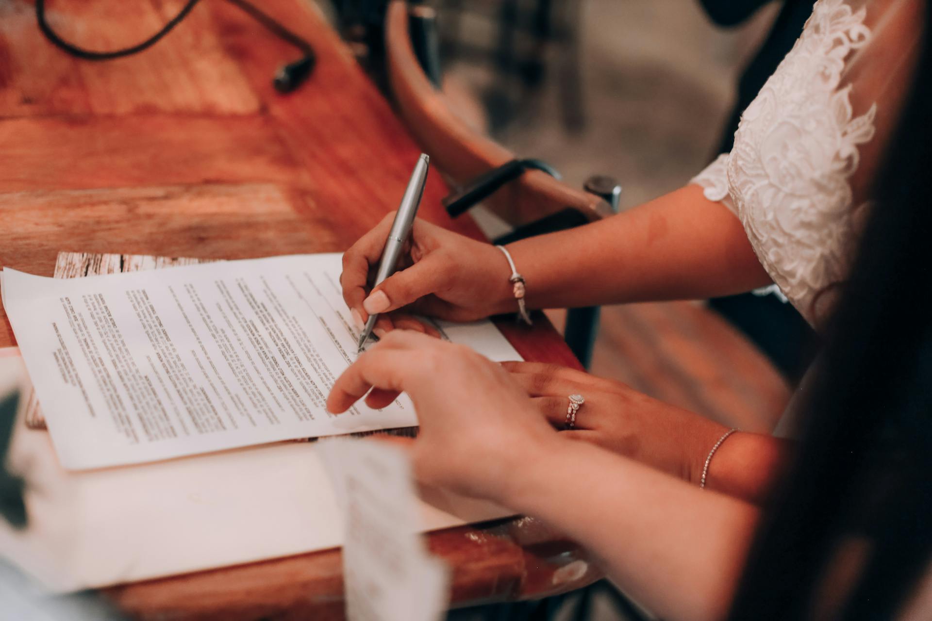 Hands signing an important document at a wooden table, symbolizing agreement and commitment.