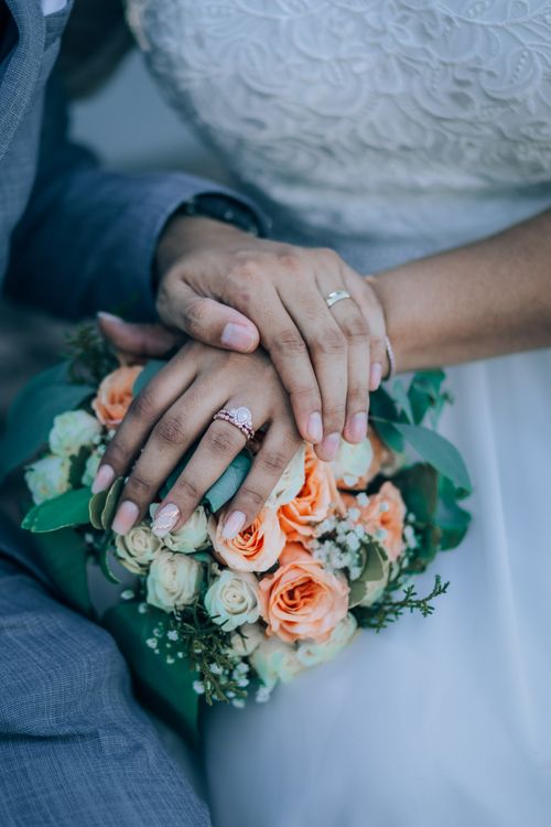 Free Close-up of newlyweds' hands with wedding rings over a bouquet, symbolizing love. Stock Photo