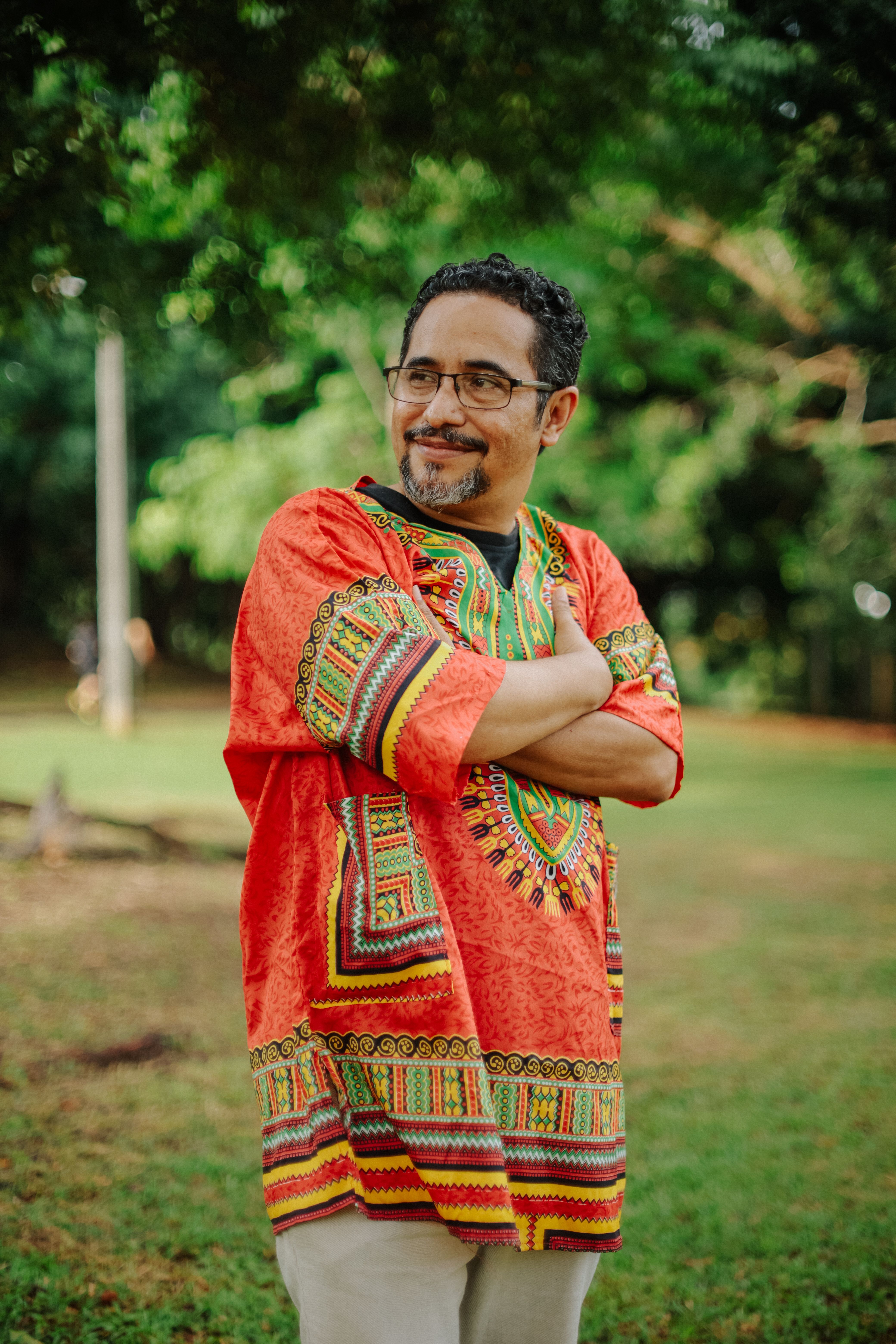 Smiling man in vibrant traditional attire standing in a park.