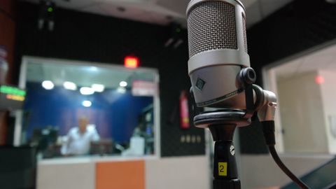 Close-up of a microphone in a recording studio with a blurred sound engineer in the background.