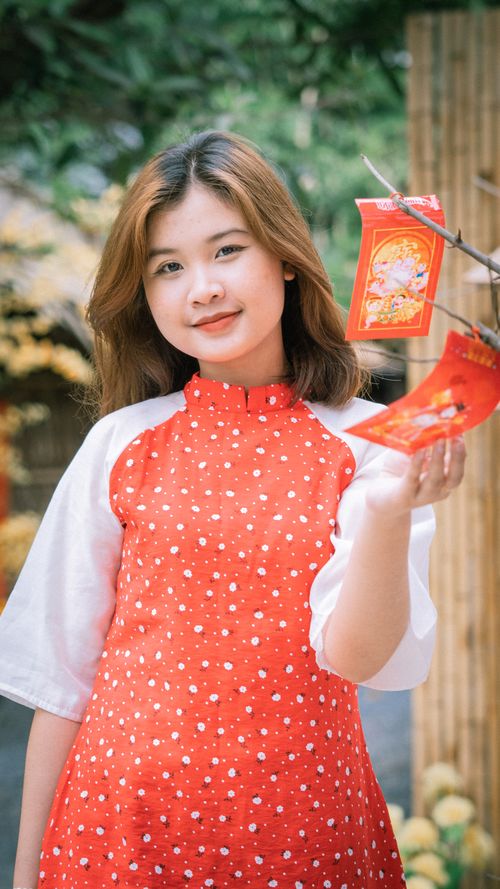 Free Asian woman in traditional clothing celebrating Lunar New Year outdoors with red envelopes. Stock Photo