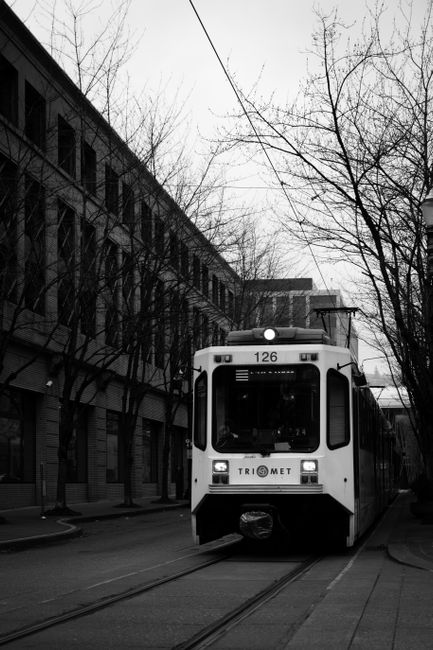 A black and white photo of a tram passing through an urban cityscape surrounded by buildings.