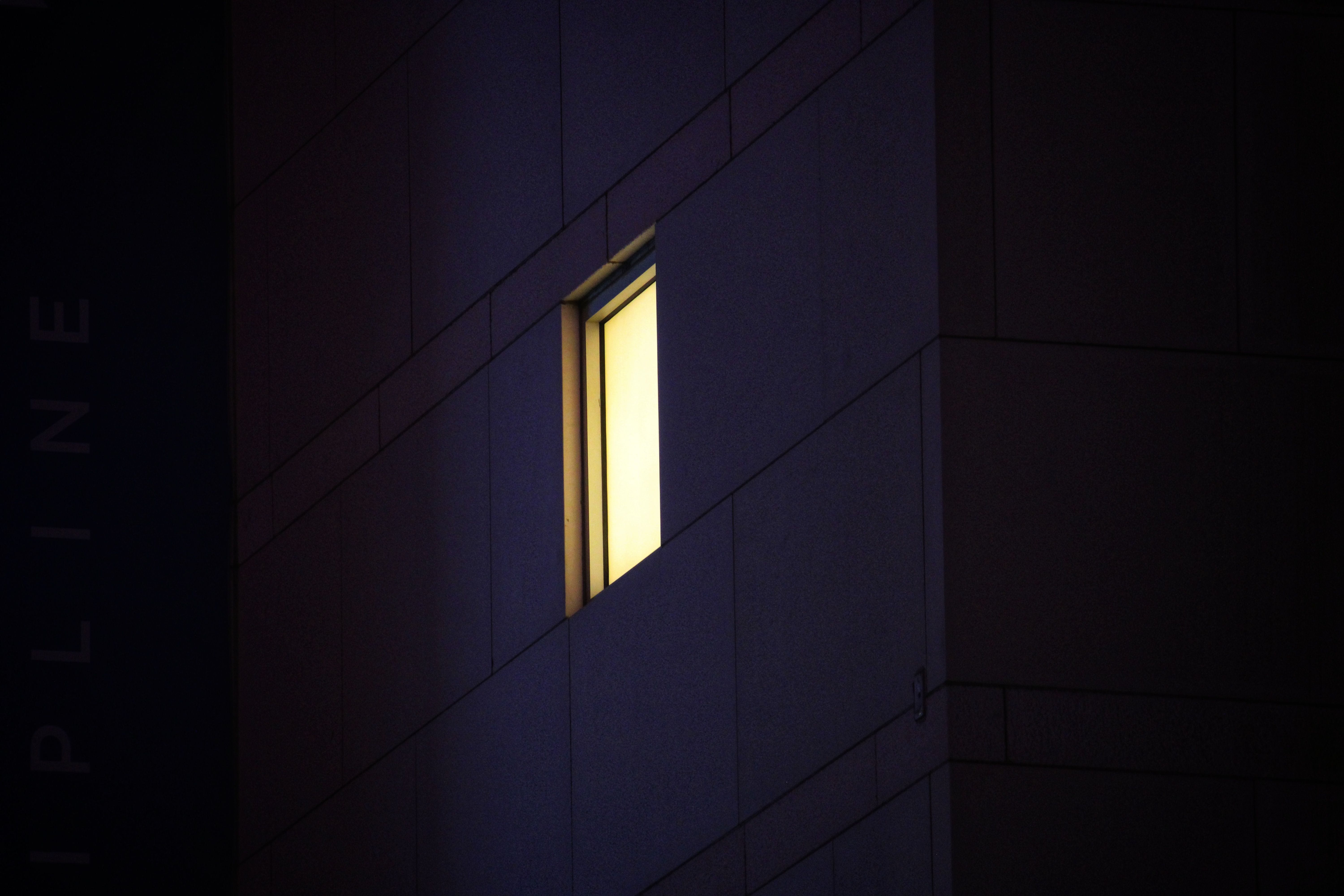 A glowing window lights up the facade of a modern urban building during the night.