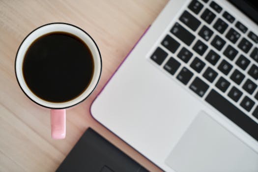 Overhead view of a pink coffee mug and laptop on a wooden desk, perfect for productivity.