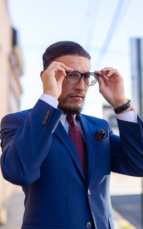 Free A confident man adjusts his eyeglasses while wearing a blue suit, showcasing urban fashion. Stock Photo