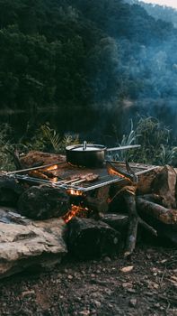 A serene outdoor cooking setup with a pot over a campfire next to a tranquil river.