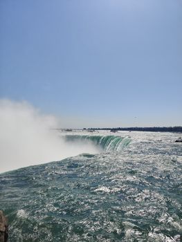 Experience the majestic Niagara Falls with clear blue skies and shimmering water cascades.