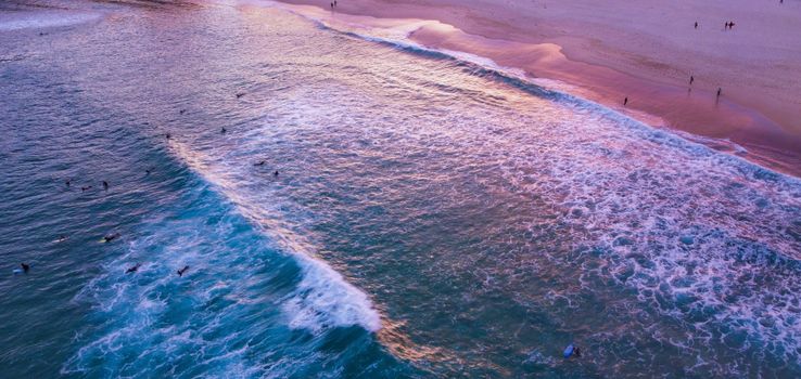 Aerial view of surfers riding waves at Bondi Beach, Australia, during a vibrant sunset.