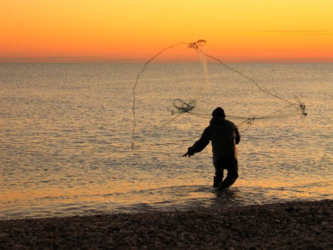 Silhouetted fisherman casting net into the Adriatic Sea at sunset in Roseto degli Abruzzi, Italy.
