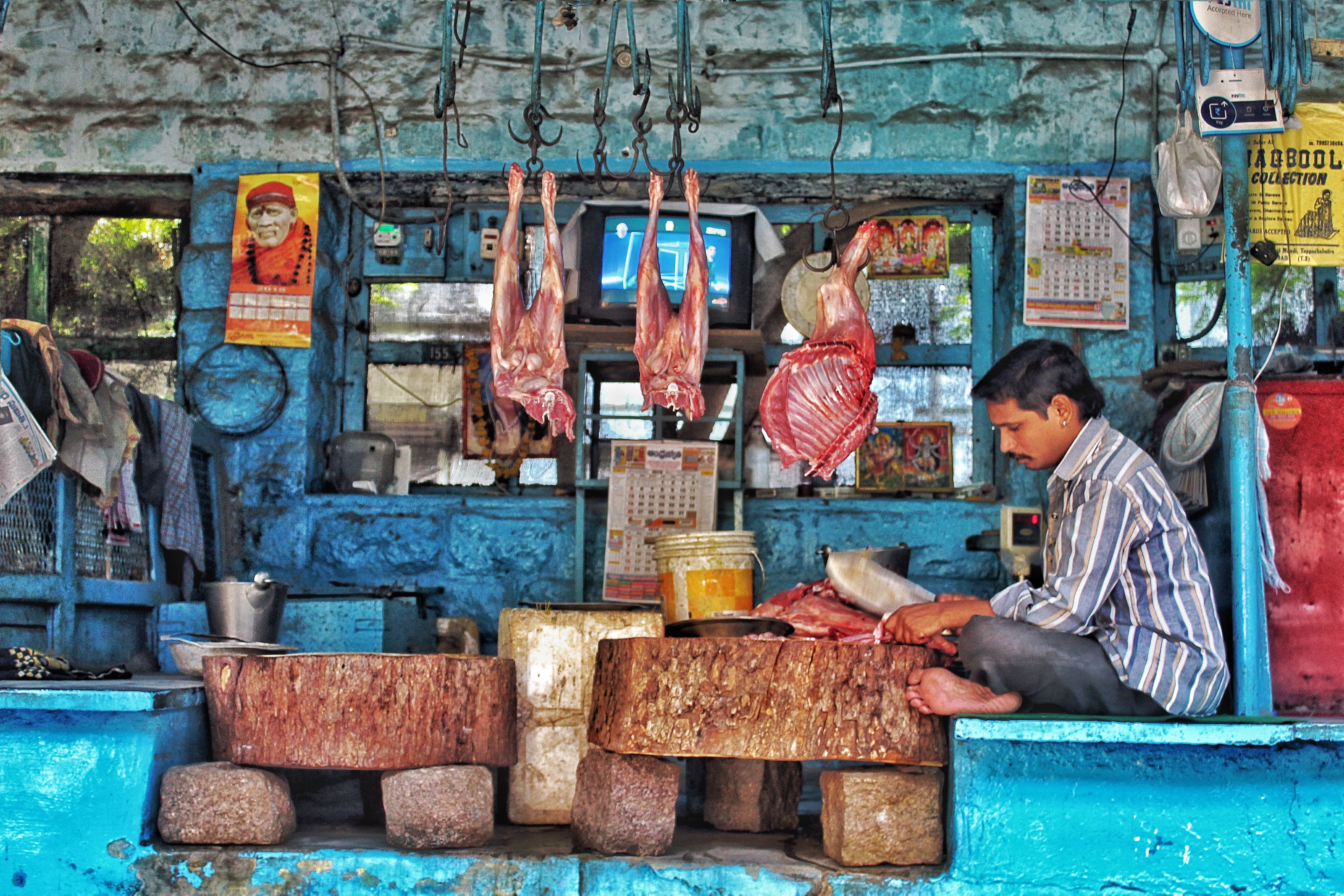 A butcher working in a rustic shop with hanging meats and blue walls.