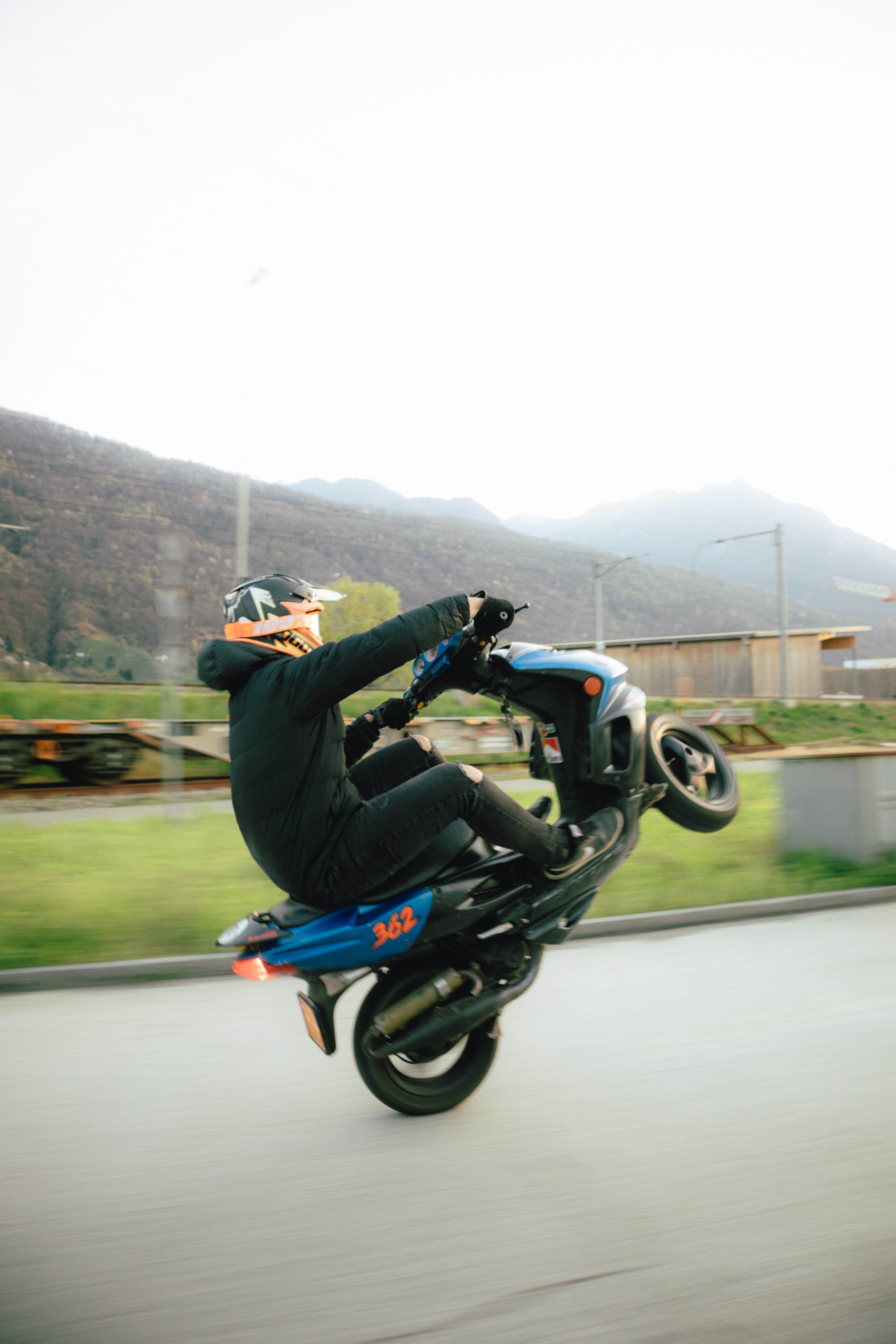 Dynamic shot of a man on a motor scooter performing a wheelie outdoors in Cadenazzo, Switzerland.