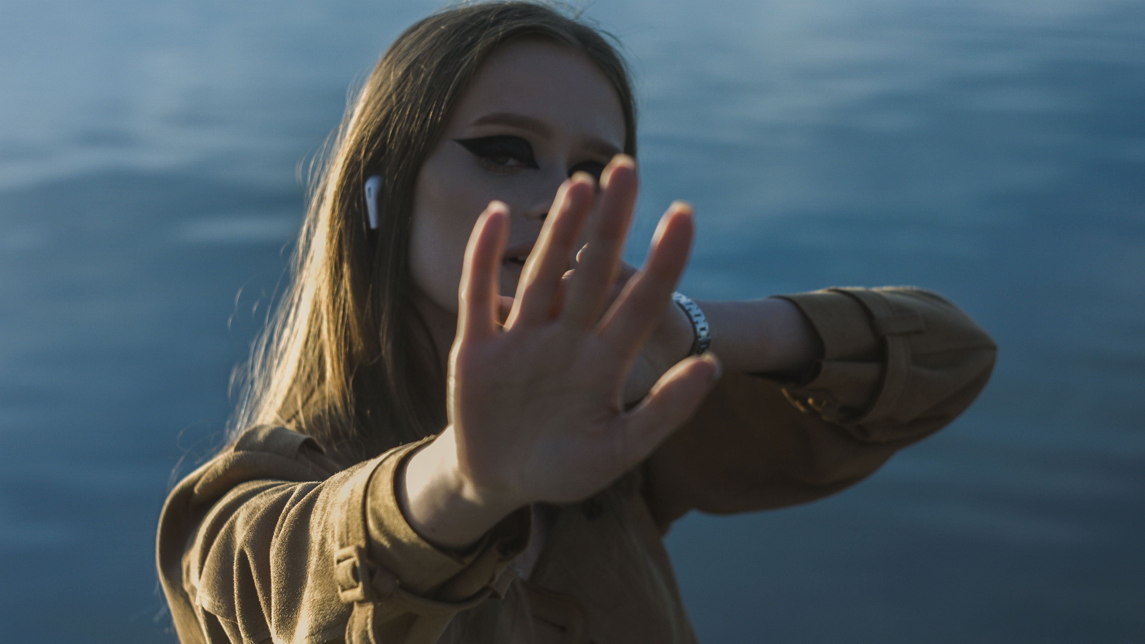 A young woman extends her hand towards the camera, set against a serene outdoor backdrop.