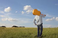 一名男子拿着吉他，穿过宁静的草地，头顶是晴朗的蓝天