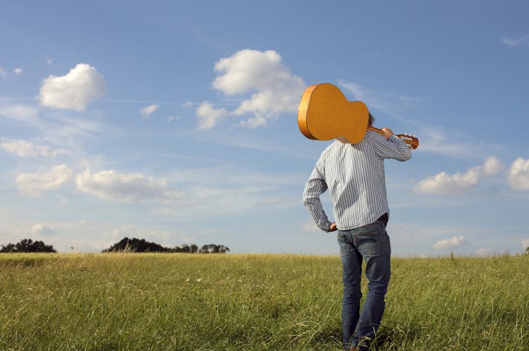 Man In Grey Long Sleeve And Blue Denim Jeans Carrying Acoustic Guitar