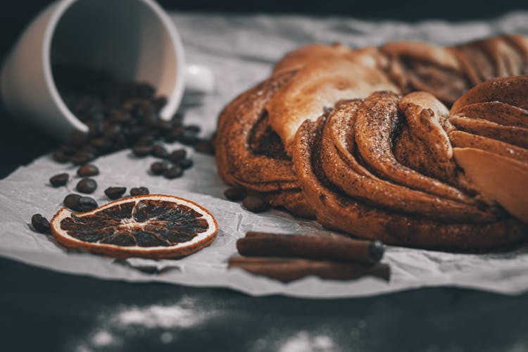 Kringle Next To Scattered Coffee Beans Cinnamon Sticks And A Slice Of Dried Orange