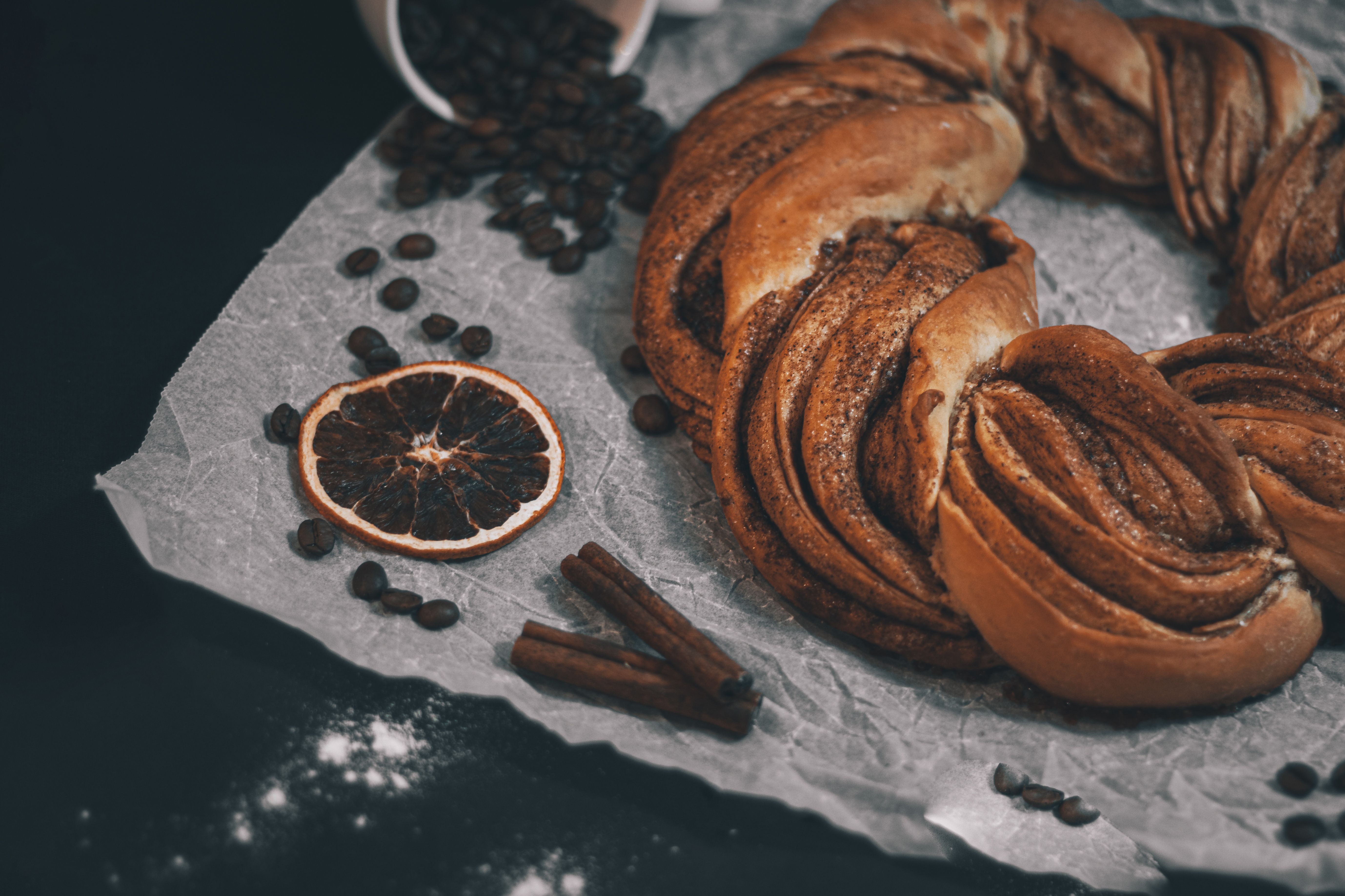 A rustic cinnamon kringle surrounded by coffee beans and dried orange for a cozy bakery setting.