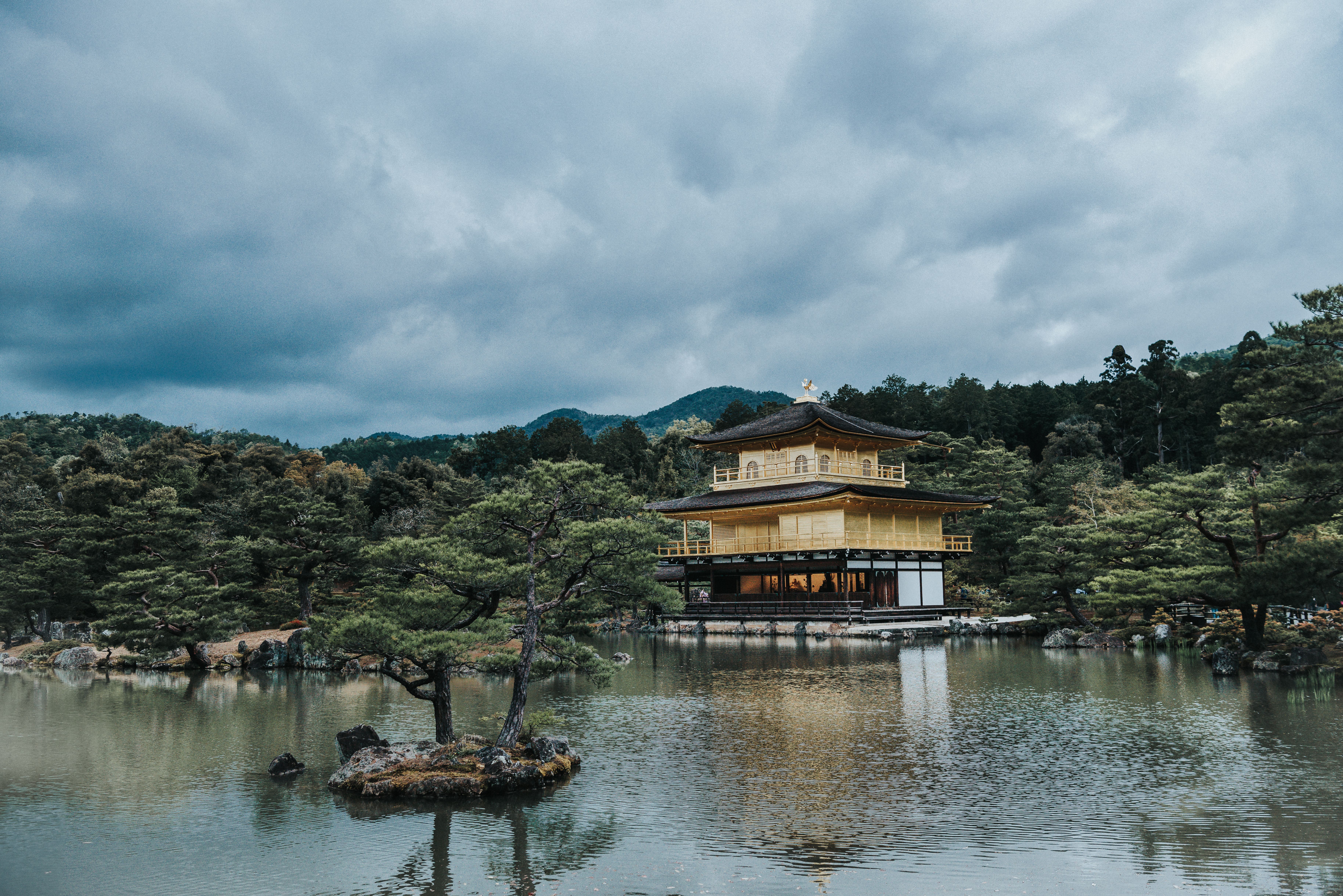 Kinkaku-ji Pavilion in Kyoto, Japan, seen over a serene pond with surrounding forest.