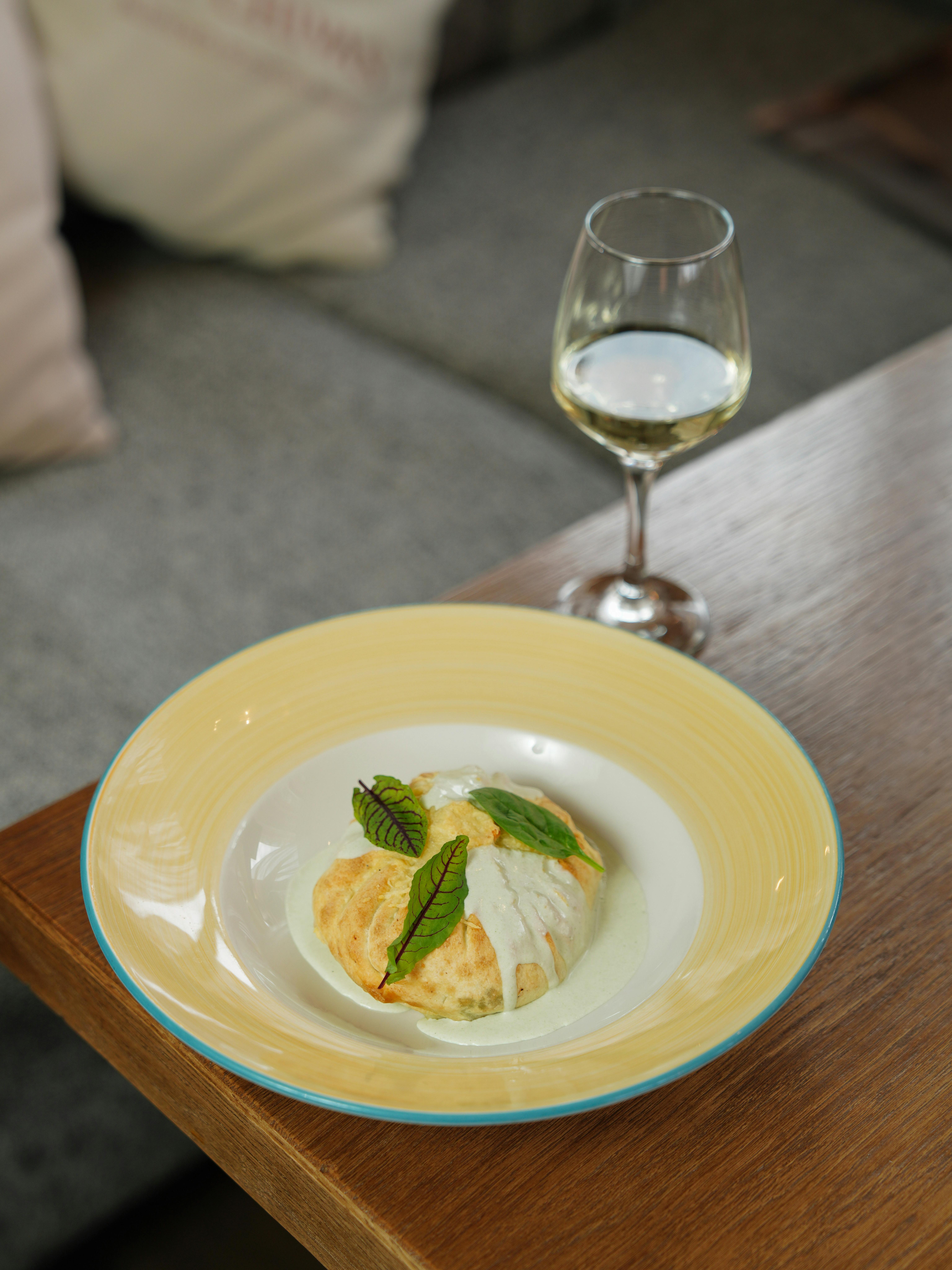 Delicious gourmet dish with a glass of wine on a wooden table in a stylish indoor setting.