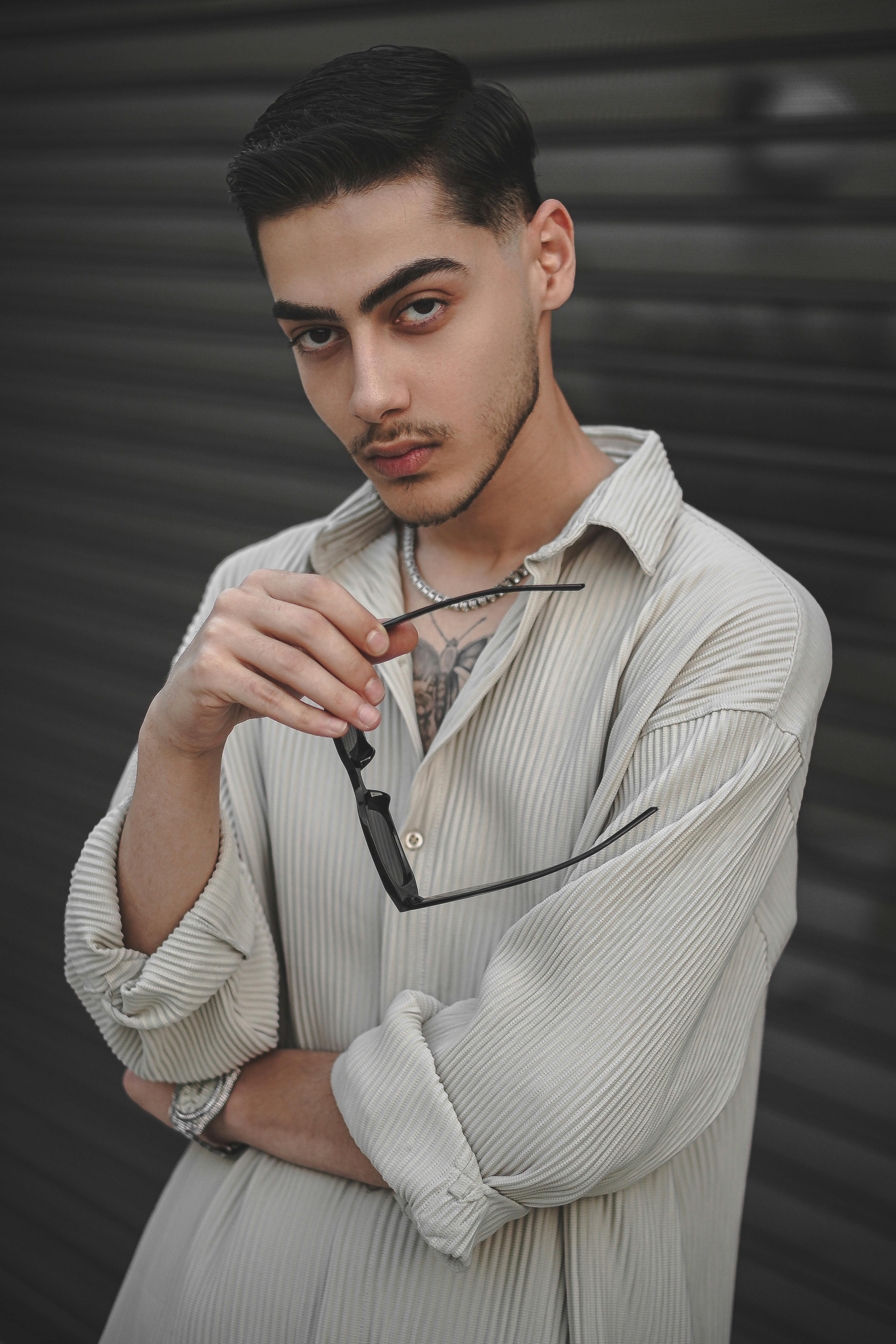 Stylish young man posing with sunglasses, exuding a trendy and fashionable vibe in a portrait setting.