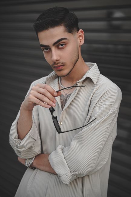 Stylish young man posing with sunglasses, exuding a trendy and fashionable vibe in a portrait setting.