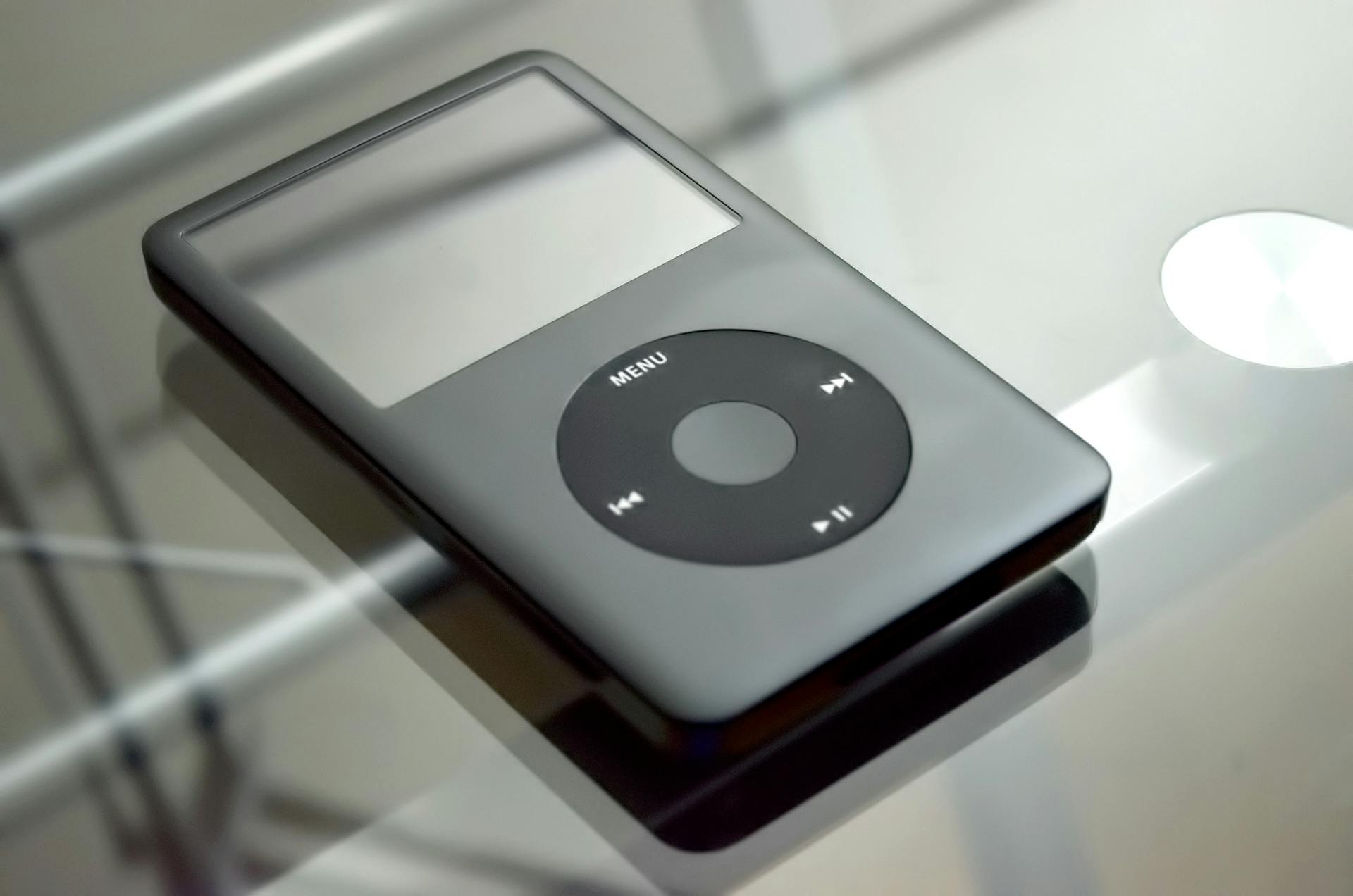 Close-up of a vintage MP3 player on a reflective glass table, showcasing its design.