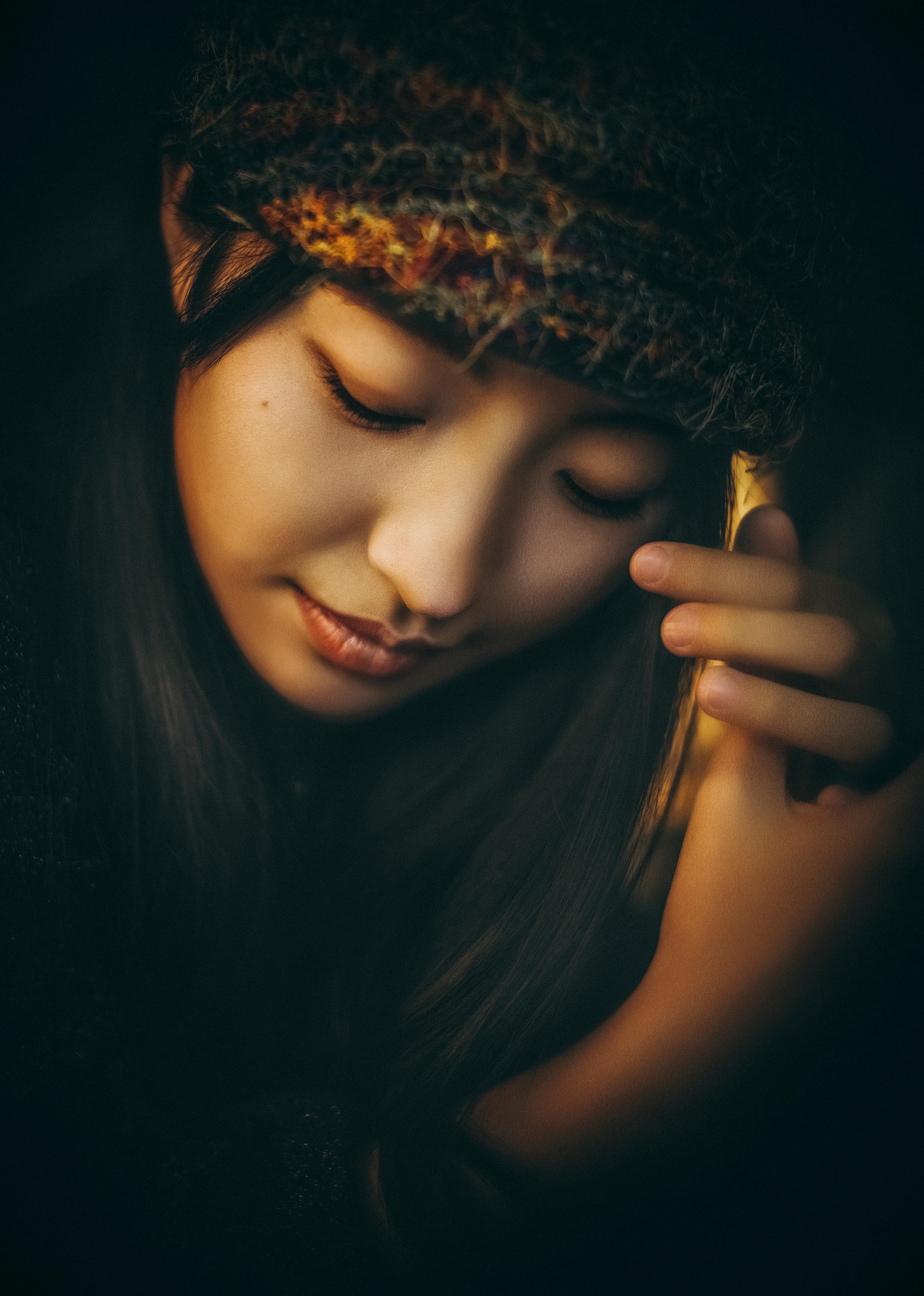 A thoughtful portrait of an Asian woman wearing a textured headband and looking downward.