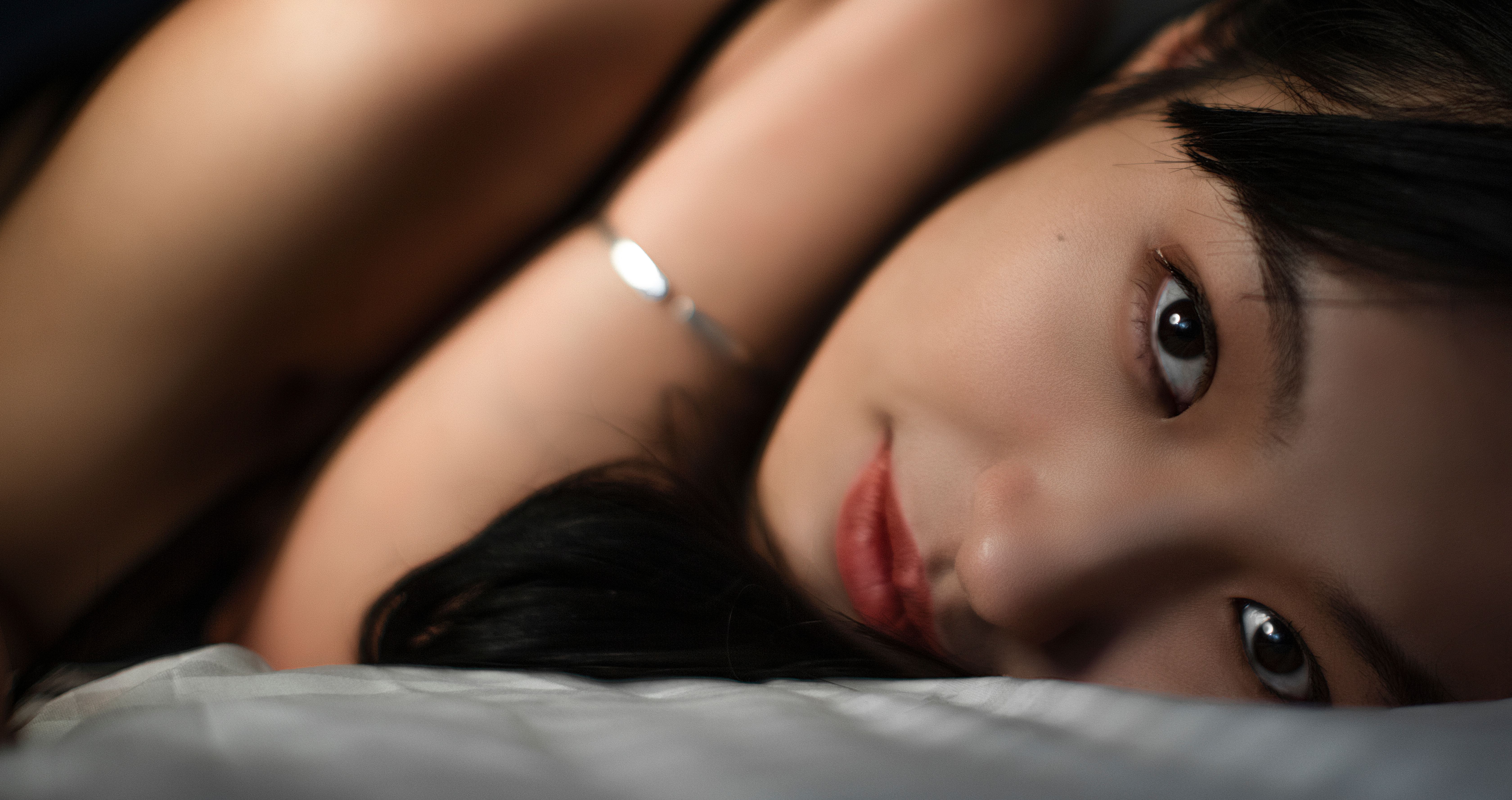 Intimate close-up portrait of a woman lying on a bed, emphasizing her serene expression and natural beauty.