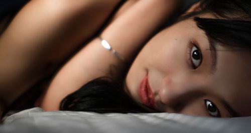 Free Intimate close-up portrait of a woman lying on a bed, emphasizing her serene expression and natural beauty. Stock Photo
