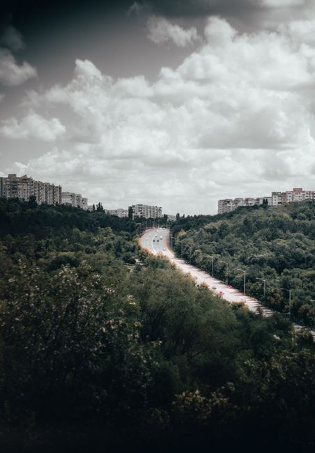 Aerial view of Chișinău showcasing lush greenery, modern buildings, and a winding road under a cloudy sky.