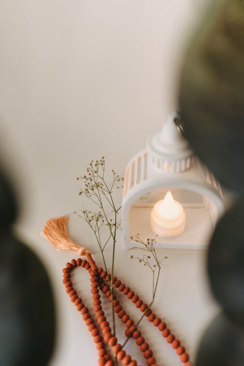 A Necklace with Orange Beads, a Candle and a Delicate Twig with Flowers Lying on White Surface