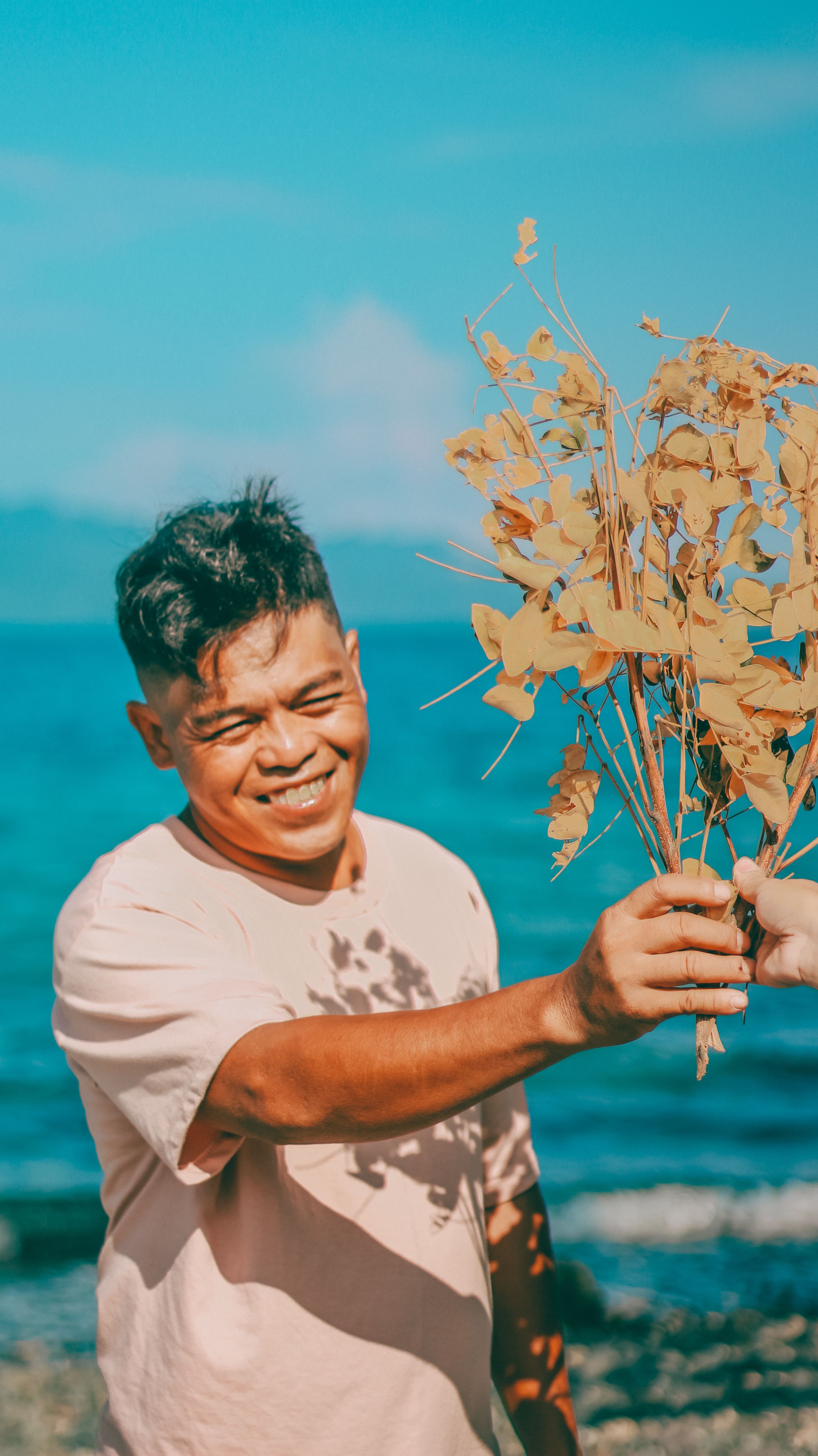 A cheerful man receives a bouquet of dry flowers on a sunny beach day.