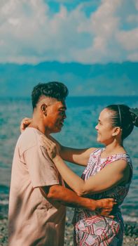 A couple shares a warm embrace by the ocean under a sunny sky.