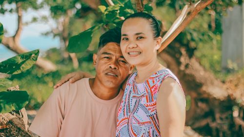 Free Smiling couple embracing under trees, enjoying a sunny day outdoors. Stock Photo