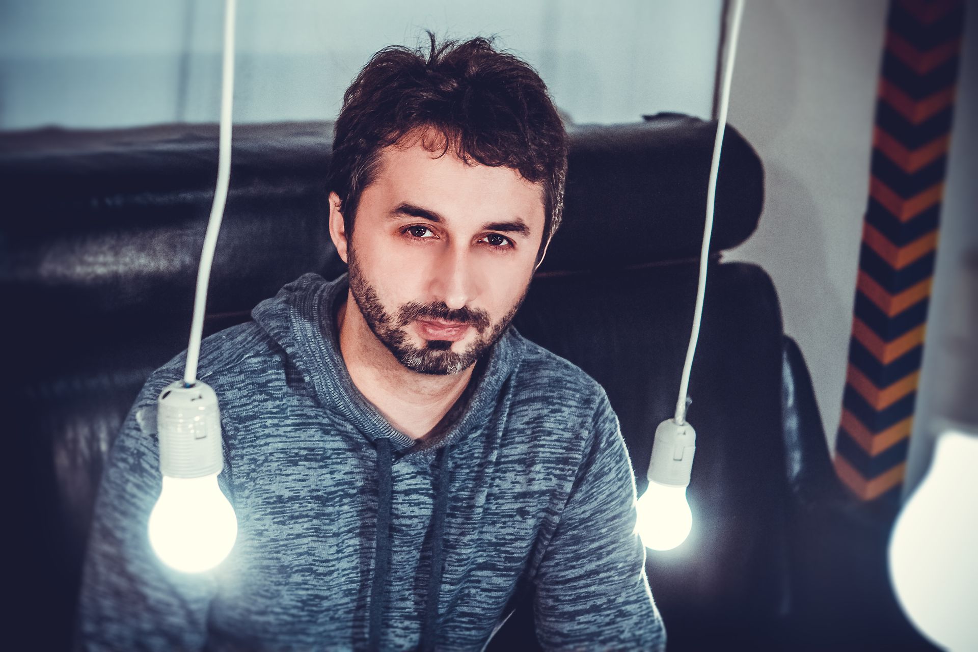 A man in a hoodie lit by hanging light bulbs, creating a moody atmosphere.