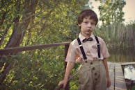 一个身着复古服装的迷人小男孩在乡村桥边摆出姿势，展现经典风格