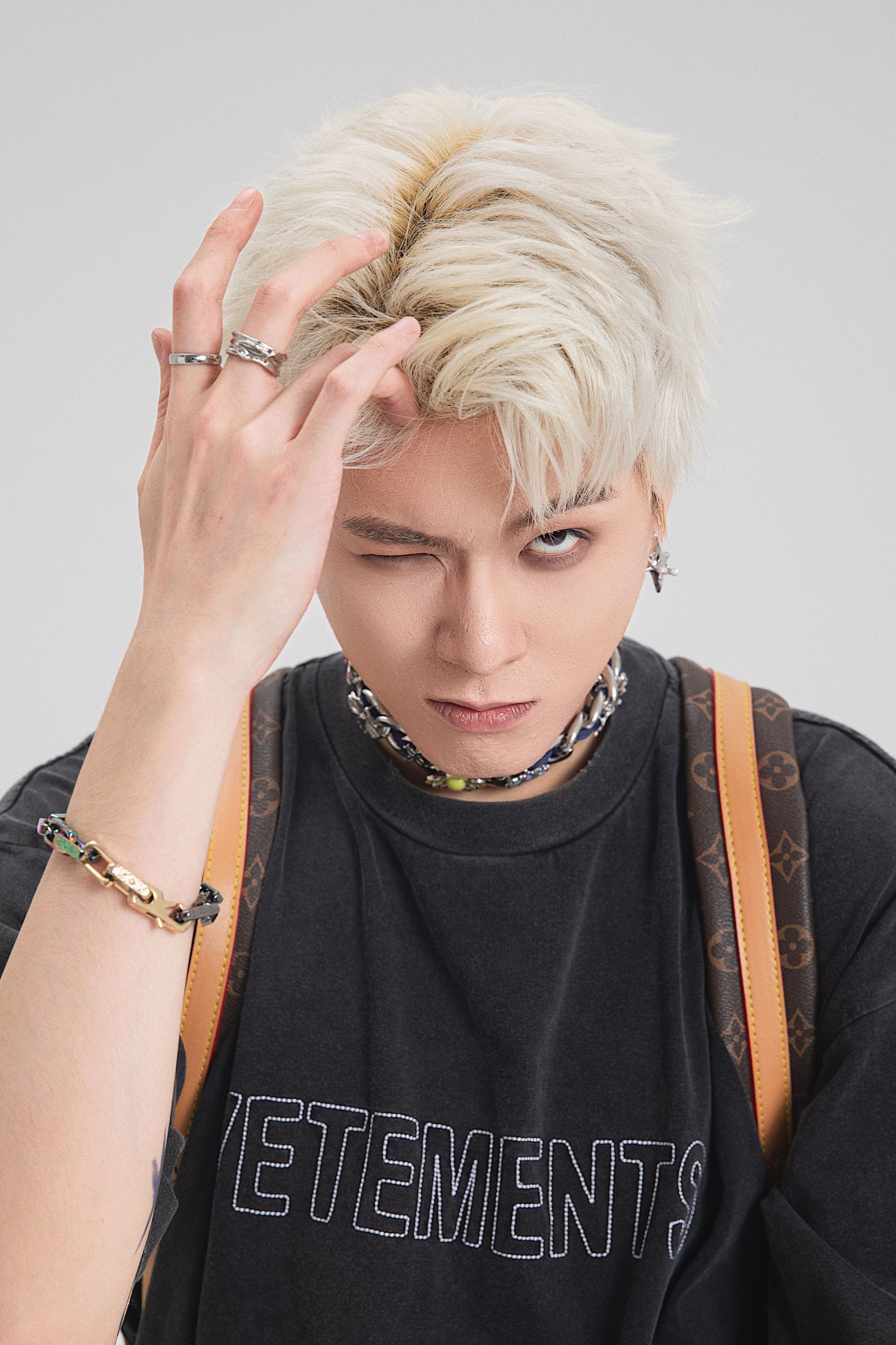 Striking portrait of an Asian male model with blonde hair in a stylish pose against a white background.
