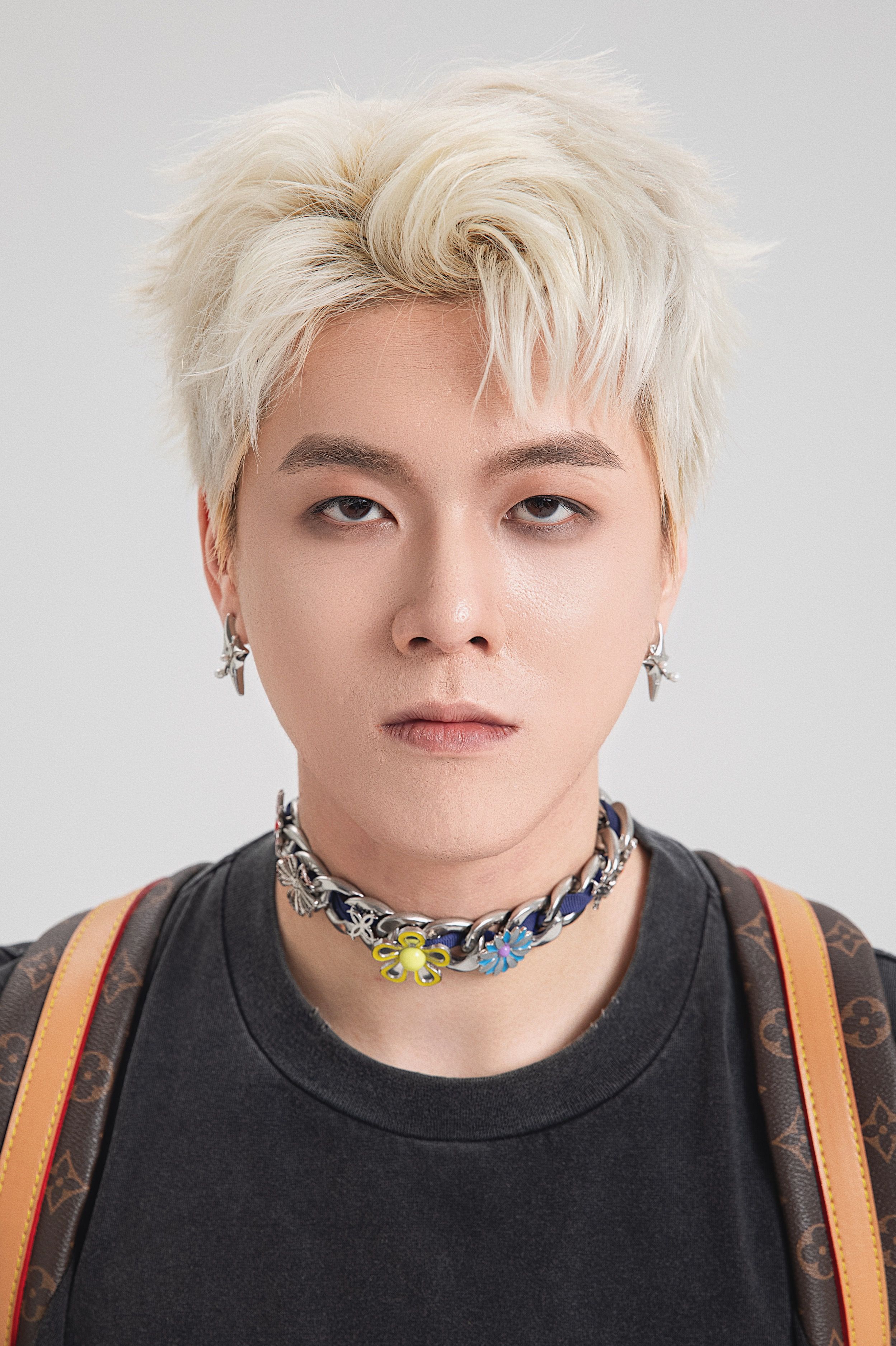Stylish portrait of a young man with dyed hair and bold accessories on a white background.